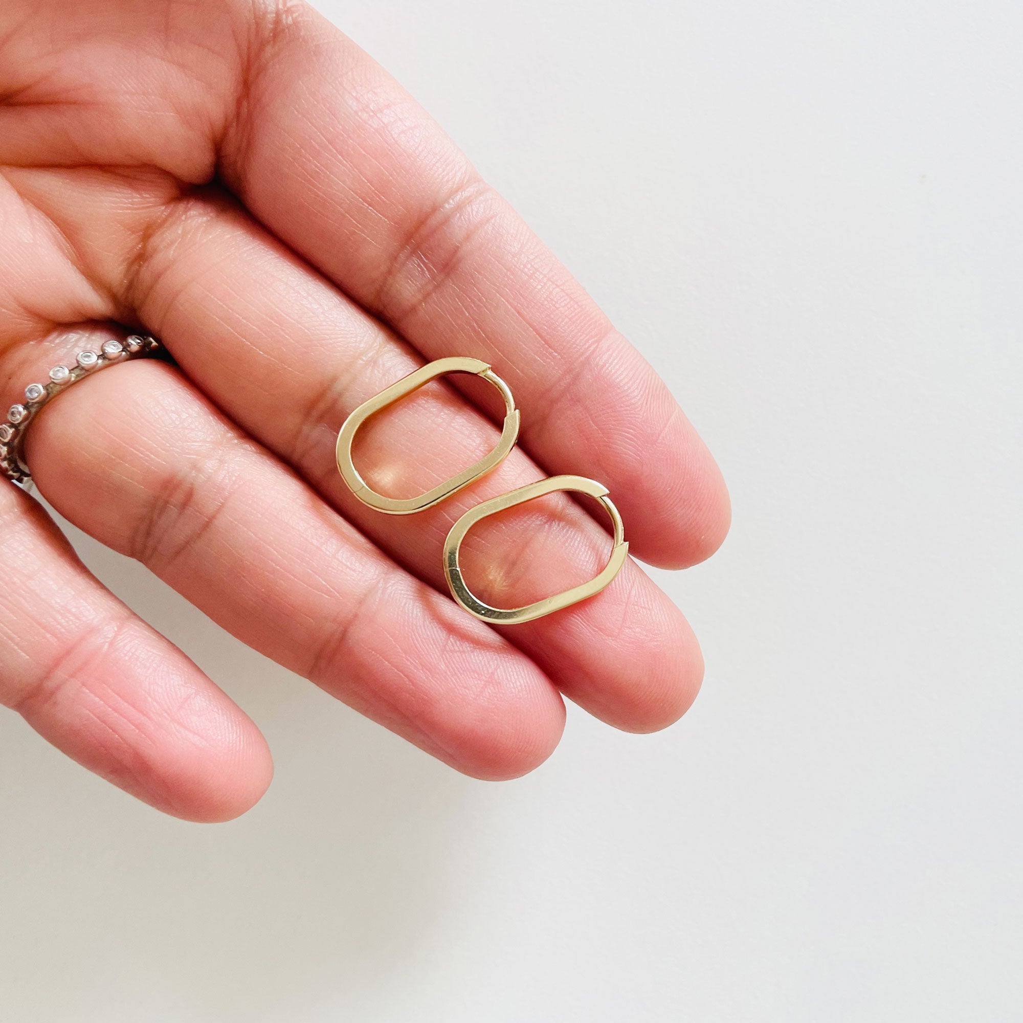 Long oval huggie hoops on hand