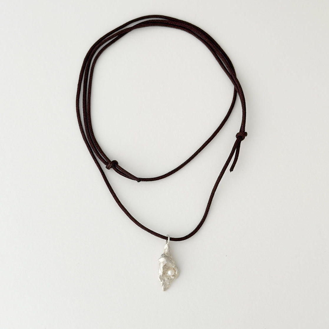 A dark brown multi-strand cord necklace with an irregular, organic silver pendant, displayed on a clean white background.