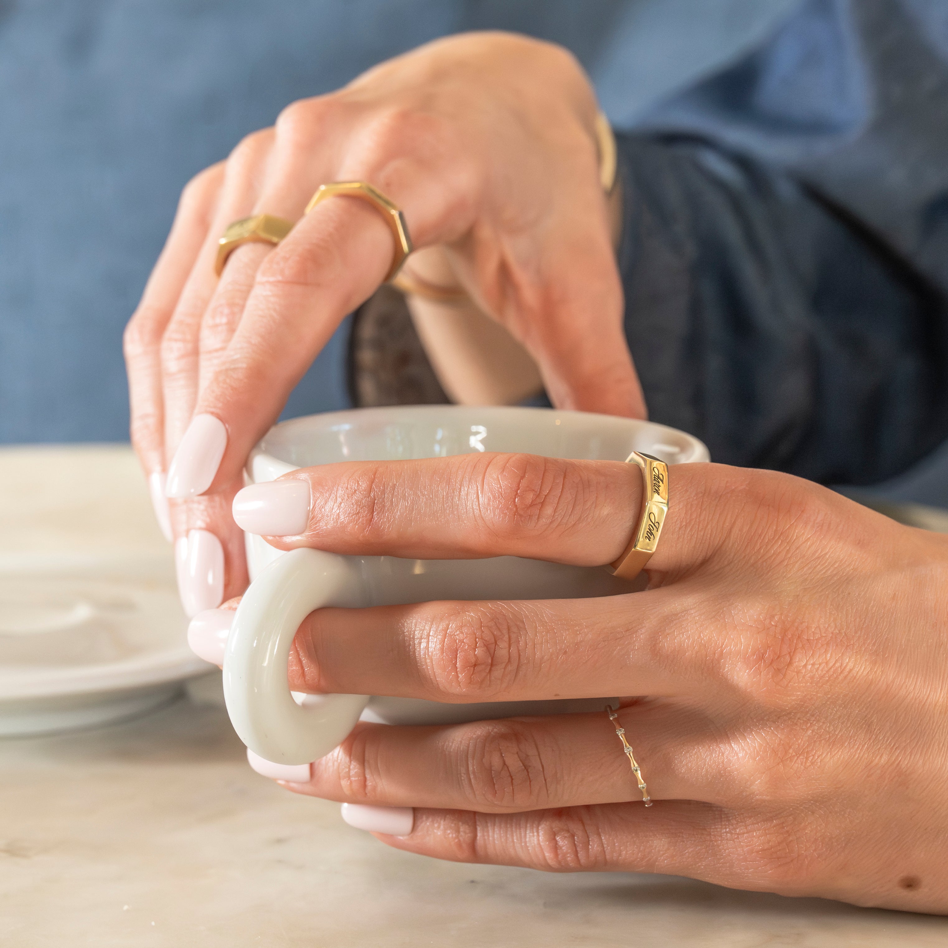 Close-up of hands holding a white ceramic cup with gold rings on fingers.