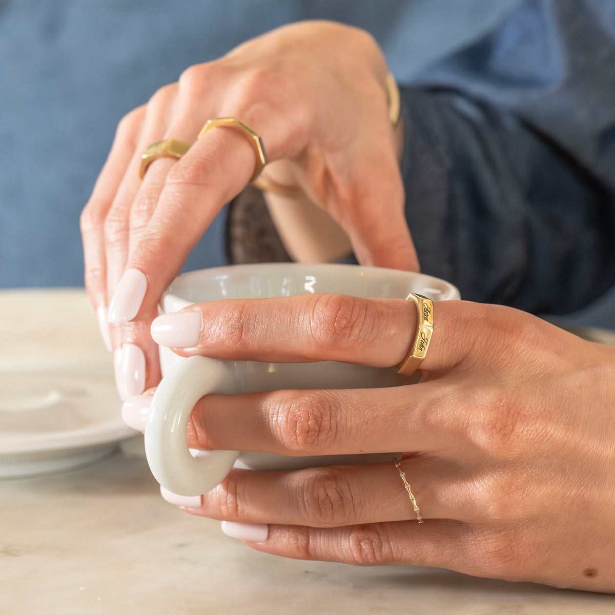 Close-up of hands holding a white ceramic cup with gold rings on fingers.