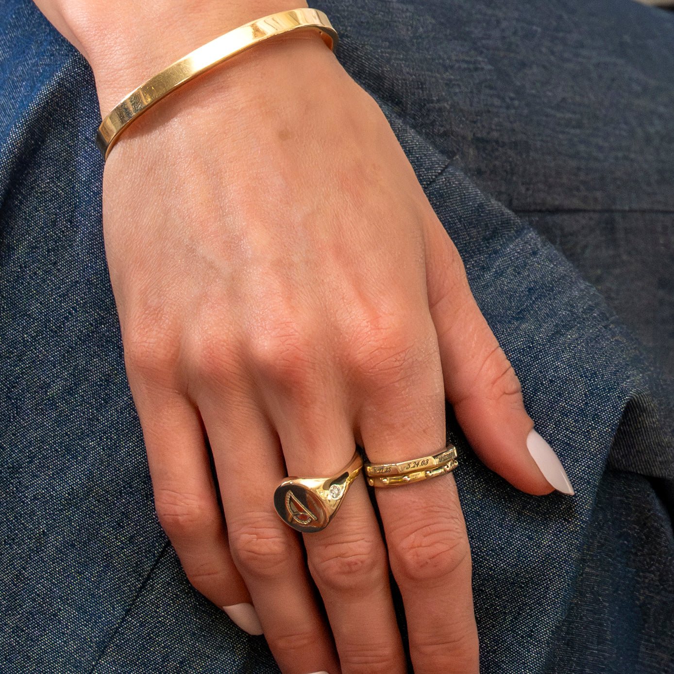 Hand wearing gold rings and a bracelet on a denim background